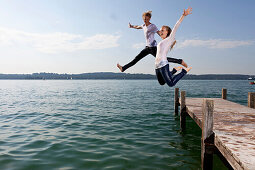 Junges Paar springt von Bootssteg in Starnberger See, Bayern, Deutschland