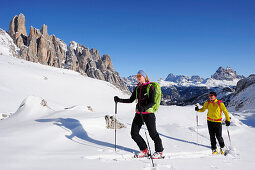 Young woman and young man ascending with crosscountry skis to Corno d'Angolo, Tre Cime di Lavaredo in background, Corno d'Angolo, Cortina, Veneto, Dolomites, Italy, Europe