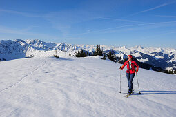 Woman with crosscountry skis ascending to Gebra, Kitzbuehel range in background, Gebra, Kitzbuehel range, Tyrol, Austria, Europe