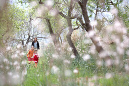 Zwei Mädchen laufen über Blumenwiese, Frau im Hintergrund, Esporles, Mallorca, Balearen, Spanien