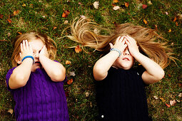 Two Young Girls Laying on Grass and Hiding Eyes