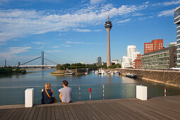 Paar sitzt auf einer Brücke am Medienhafen, Blick auf Rheinturm und Neuen Zollhof, Düsseldorf, Nordrhein-Westfalen, Deutschland, Europa