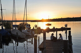 Menschen auf einem Steg am Ammersee bei Sonnenuntergang, Herrsching, Oberbayern, Bayern, Deutschland, Europa