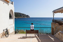 Rennradfahrer sitzt auf einer Bank am Mittelmeer, Sant Elm, Mallorca, Balearische Inseln, Spanien