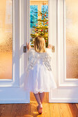 Girl wearing an angel costume looking through a sliding door, christmas tree in background, Hamburg, Germany