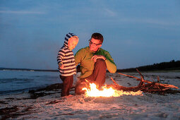 Father and son (2 years) at a campfire at beach in the evening, Schaabe, Island of Ruegen, Mecklenburg-Western Pomerania, Germany