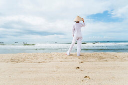 Frau mit vietnamesischer Kleidung und Strohhut blickt auf das Meer mit Fischerbooten, Strand von Mui Ne, Südvietnam, Vietnam, Asien