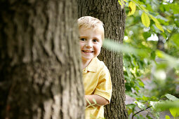 Boy (3 years) standing behind a tree