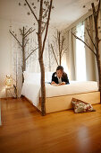 Junge Frau liegt mit einem Buch auf einem Bett, Hotel Maison Moschino, Mailand, Lombardei, Italien
