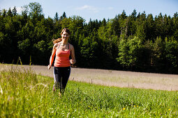 Junge Frau joggt über eine Wiese, Oberbayern, Deutschland