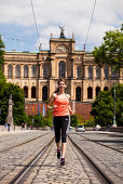 Young woman jogging over Maximilian bridge, Maximilianeum in background, Munich, Bavaria, Germany