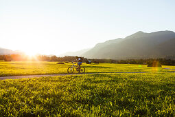 Mountainbiker fährt an Wiesen mit Heustadel vorbei, Grainau, Bayern, Deutschland