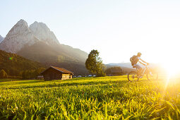 Mountain biker passing meadow with hay barns, Grainau, Bavaria, Germany
