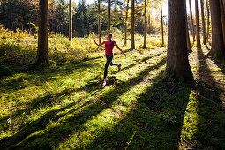 Junge Frau joggt durch herbstlichen Wald, Berg, Bayern, Deutschland