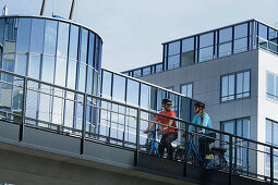 Couple with e-bikes passing a bridge, Munich, Bavaria, Germany