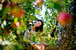 Junge Frau sitzt in einem Apfelbaum, Steiermark, Österreich