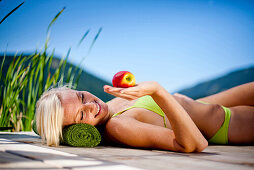 Young woman with an apple lying on a jetty, Fladnitz an der Teichalm, Styria, Austria
