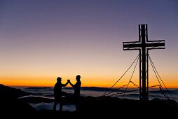 Two hikers at summit of Hochschwab mountain at sunrise, Hochschwab, Styria, Austria