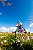 Junge Frau im Dirndl fährt mit einem Mountainbike über eine Wiese, Duisitzkar, Planai, Steiermark, Österreich