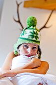 Young woman wearing a woolly hat hugging a pillow, Styria, Austria
