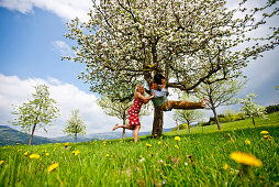 Frau schubst Mann auf einer Schaukel in einem Apfelbaum an, Stubenberg, Steierermark, Österreich