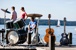 Musikinstrumente auf einem Steg am Starnberger See, drei Personen im Hintergrund, Bayern, Deutschland