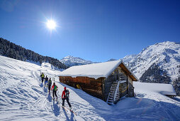 Gruppe von Skitourengehern gehen an verschneiter Almhütte vorbei, Hoher Kopf, Tuxer Alpen, Tirol, Österreich