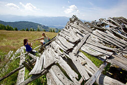 Two female hikers resting near the remains of a wooden lodge, Nockberge, Carinthia, Austria