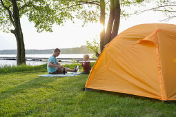 Vater und Sohn beim Abendbrot vor einem Zelt am Seeufer, Lychen, Naturpark Uckermärkische Seen, Uckermark, Brandenburg, Deutschland