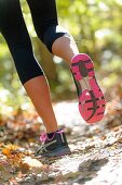 The back view of legs of a woman wearing work-out clothing jogging on a trail in a forest setting in the fall