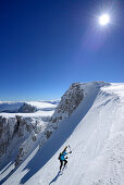 Female backcountry skier ascending through snow-covered cirque at Monte Sirente, Maiella range in background, Valle Lupara, Abruzzo, Italy