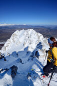 Female backcountry skier standing at edge of a rocky downhill run, Canale Maiori, Monte Sirente, Abruzzo, Italy