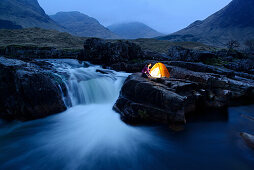 Frau sitzt vor einem beleuchtetem Zelt, Glen Etive, Highlands, Schottland, Großbritannien