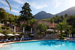 Couple walking along a hotel pool, Serra de Tramuntana in background, Deia, Majorca, Spain