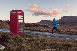 Junger Mann joggt an einer rote Telefonzelle vorbei, Trotternish Halbinsel, Isle of Skye, Schottland, Großbritannien