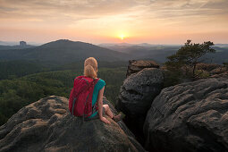 Junge Frau sitzt auf einem Felsen und genießt Sonnenuntergang, Nationalpark Sächsische Schweiz, Sachsen, Deutschland