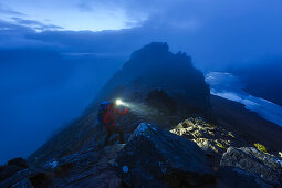 Junge Frau mit Stirnlampe steigt in der Dämmerung auf den Gipfel des Stac Pollaidh, Assynt, Schottland, Großbritannien