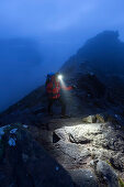 Junge Frau mit Stirnlampe steigt in der Dämmerung auf den Gipfel des Stac Pollaidh, Assynt, Schottland, Großbritannien