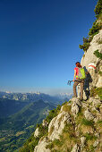 Frau steigt über Steig Steinerne Jäger zum Hochstaufen auf, Reiteralm und Loferer Steinberge im Hintergrund, Chiemgauer Alpen, Chiemgau, Oberbayern, Bayern, Deutschland