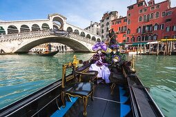 A masked couple in a gondola in front of the Rialto Bridge at the carnival in Venice, Italy, Europe