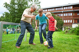 Vater, Großvater und Sohn spielen Fußball auf einem Spielplatz, Steiermark, Österreich