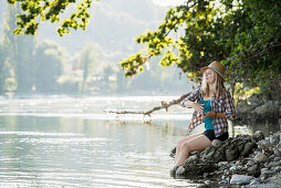 Young woman wearing a strawhat sitting at river Rhine, Rheinfelden, Baden-Wurttemberg, Germany