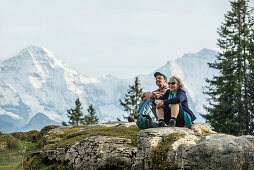 Paar rastet auf einem Felsen, Eiger, Mönch und Jungfrau im Hintergrund, Beatenberg, Berner Oberland, Kanton Bern, Schweiz