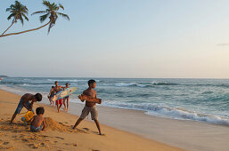 Palm trees bending over the beach, Surfer and children on the beach in the early evening, Hikkaduwa, Southwest coast, Sri Lanka