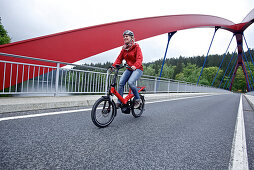 Woman riding an electric bicycle passing a bridge, Tanna, Thuringia, Germany