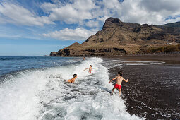 Children playing in the breakers, Faneqe mountain and Playa del Risco, beach, near Agaete, Atlantic ocean, Natural Preserve, Parque Natural de Tamadaba, UNESCO Biosphere Reserve, West coast, Gran Canaria, Canary Islands, Spain, Europe