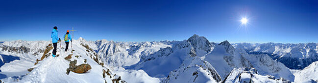 Two female back-country skiers beside Kuhscheibe summit cross, Stubai Alps, Tyrol, Austria