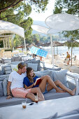 Couple sitting on a bench while reading a book in a beach bar, Vourvourou, Sithonia, Chalkidiki, Greece