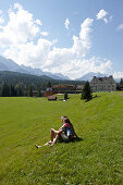 Paar sitzt auf einer Wiese, Schloss Kranzbach im Hintergrund, Klais, Krün, Oberbayern, Bayern, Deutschland
