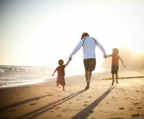 Father and sons walking hand in hand on beach at sunset